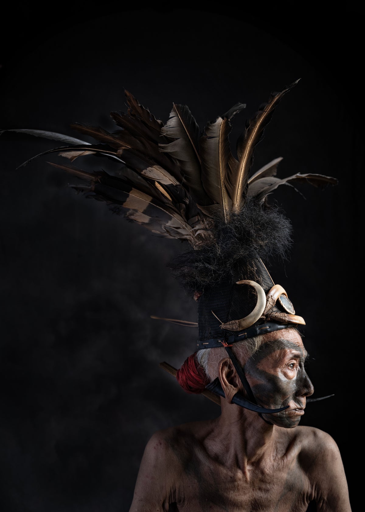 Person wearing a traditional headdress with feathers against a black background